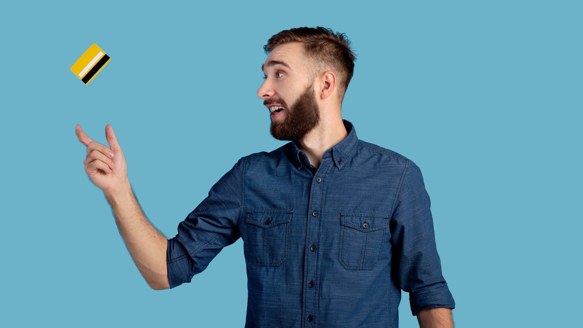 Millennial hipster guy catching credit card on blue studio background, panorama. Contactless payment