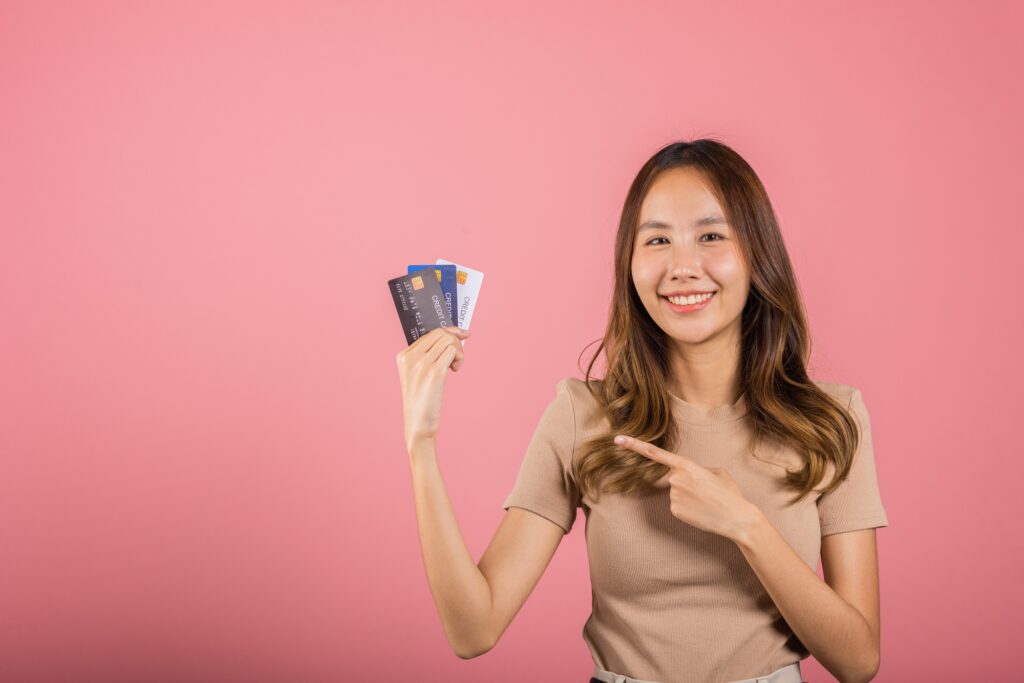 Portrait of Asian young woman holding bank card solution in hands in studio shot isolated on pink